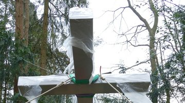 Man sieht ein großes Kreuz aus Metall in Schräglage.